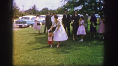 1961: lady in white dress helping a small child to walk at a family event