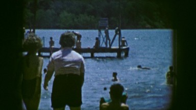 1961: the scene shows people swimming in a beach and a lifeguard overlooks