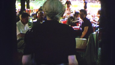 1963: a group of people dining outdoors around tables when a uniformed worker