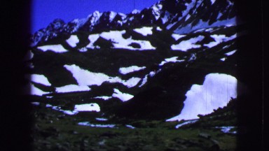 1963: large green and rocky mountains covered by snow as seen from a train