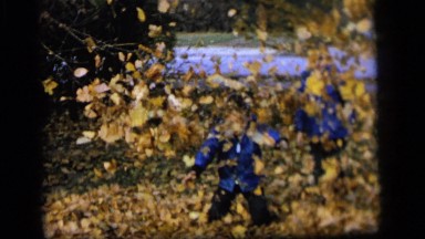 1964: two boys in blue jackets standing in a leaf pile, one throwing leaves