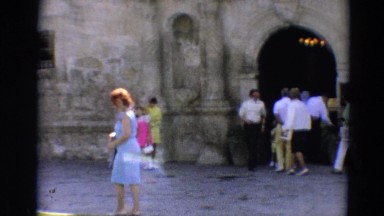 1968: a lone woman dressed in a blue outfit stolling passed a stone building