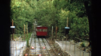 1968: a lone red train car with windows rolling on track through fenced in area