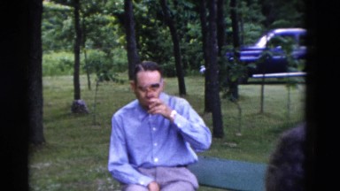 1949: two ladies relaxing on a swing in a park as a man sips his drink.