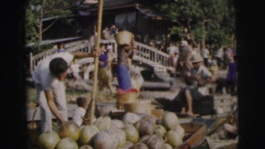 1962: people of asian decent trading goods like food on the water's edge