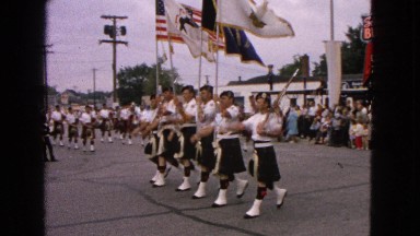 1963: a large group of men in kilts marching through the street playing