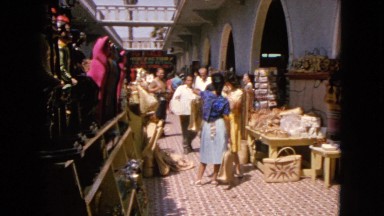 1963: men and women shopping on a side street while a little girl plays