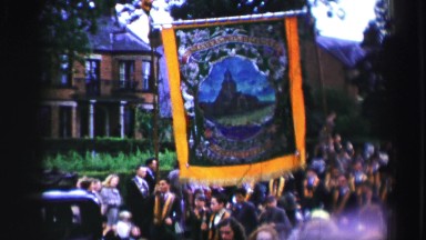 1952: people dancing and marching in parade style down a street holding a large