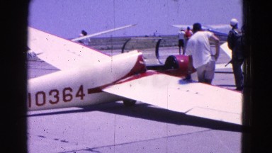 1964: small airplane taxiing around parked airplanes at an airport while pilots
