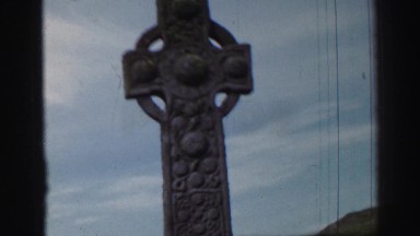 1952: Stoic cross stands tall in a rocky grassland among few passerby's..ENGLAND