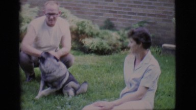 1966: A family playing with and petting a cute gray dog in the grass in front of