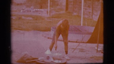 1968: a cute young boy at a campsite stirring a pot near an open fire pit