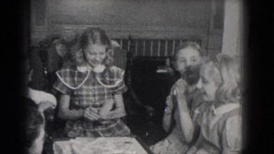 1953: a teen girl in a plaid dress reads a card and opens a gift as her friends