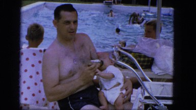 1964: a male adult in bathing attire and wearing a metal disc, holds and feeds