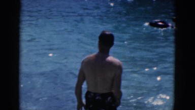 1968: two handsome young men in shorts playing in a beautiful swimming pool