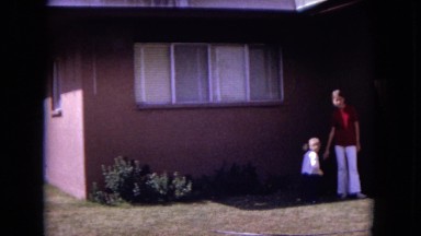 1970: A Cute Young Girl with Blonde Hair Running from the House Through the Yard