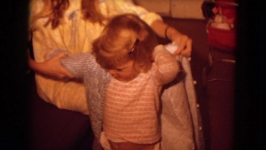 1970: woman putting on clothes on a pouty child who cannot put it on herself,