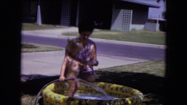 1970: baby playing in an inflatable pool watched over by mother WHITE SANDS,