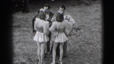 1948: men in costumes on horses with flags riding through tents on either side