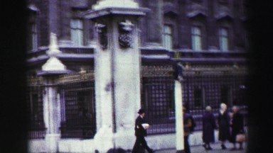 1952: people on a busy street walking past a fence and a building