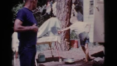 1968: boy retrieving water to treat injury on his knee while father smokes