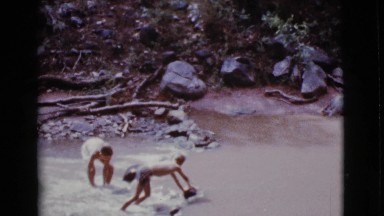 1968: two children standing in a river throwing rocks and building a damn