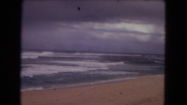 1968: little children standing on the beach watching big rolling waves. HAWAII