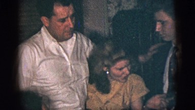 1956: Two Well-Dressed Men and a Woman Talking and Motioning as They Huddle