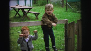 1972: toddlers playing outside while hanging on a gate. LYNBROOK, NEW YORK