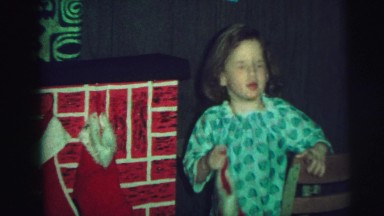 1972: girl and mother in green outfits hanging up christmas stocking.