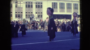 1948: three-headed costumed person walks through crowded street