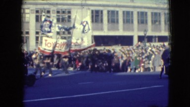 1948: people on a busy street walking in a parade as the hold up a large sign