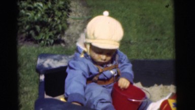 1951: baby playing outdoors in sandbox trying to pick up the sand with shovel
