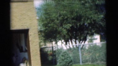 1951: the front of a brick home including the open garage with a car inside