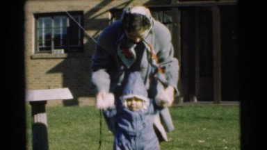 1951: mother takes child for first steps in grassy front yard wiggling his puffy