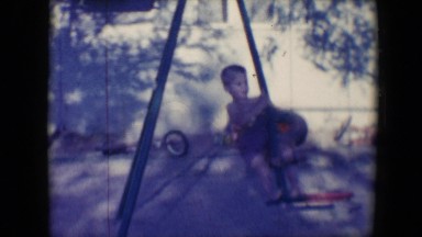 1958: children play on swings and cars in shadowy area near old tires