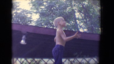 1958: a cute shirtless boy is reaching up over a fence and playing