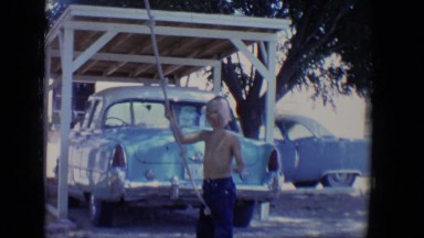 1958: a cute shirtless boy preparing to climb up a rope hanging from above
