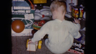 1959: a blonde little boy in gray pajamas plays with a wooden truck