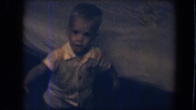 1959: smiling little child next to bed picks up and puts away his toys