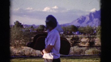 1968: Elderly Woman Holds Bundle Standing in Front of Mountain