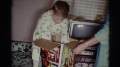 1968: a small boy in pajamas opening a present and pulling a truck from a box