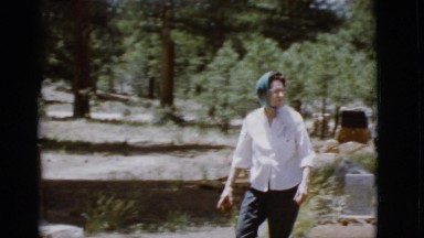 1968: a woman wearing a scarf in a cemetery walking towards a car COTTONWOOD,