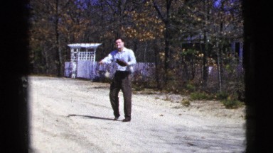1956: man smoking a cigarette plays catch and uses a baseball mitt in the street