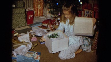 1967: a small girl on the livingroom floor excitedly opening a christmas present
