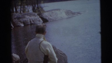 1956: man fishes at lake with woman at his side on a rocky mountain view FLORIDA