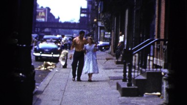 1956: Shirtless Man Escorts Woman Down City Street Arm-in-Arm