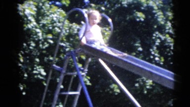 1967: little toddler has fun while playing outdoors sliding on a big slide.