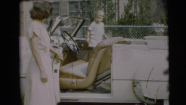 1954: a small boy plays inside a nice car as a family gathers around