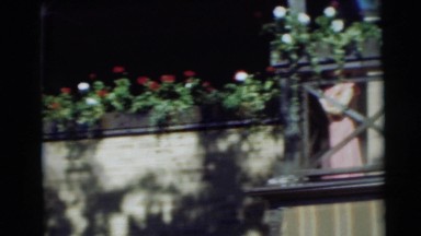 1954: woman holding child overlooks flower-covered railing while smiling